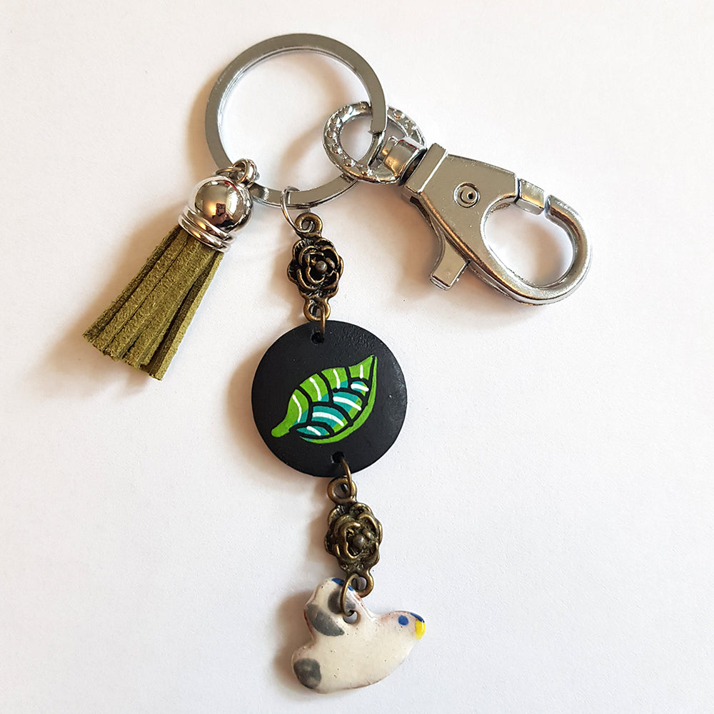 CocoFlower Handmade Bird Keychain: Green tassel, metallic bead, black leaf charm, white ceramic bird charm on silver ring