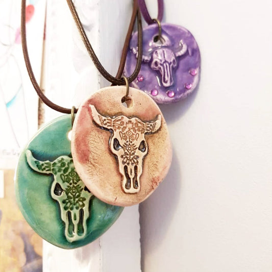 Handcrafted ceramic necklaces featuring cow skull designs, displayed against a soft background by cocoflower.