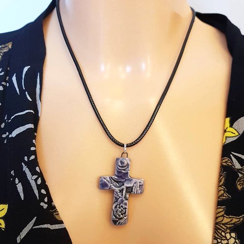 A Purple cross pendant with an intricate design hanging from a black cord 