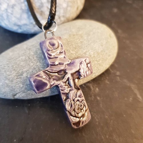 A purple-toned cross pendant with rose details resting on a wooden surface